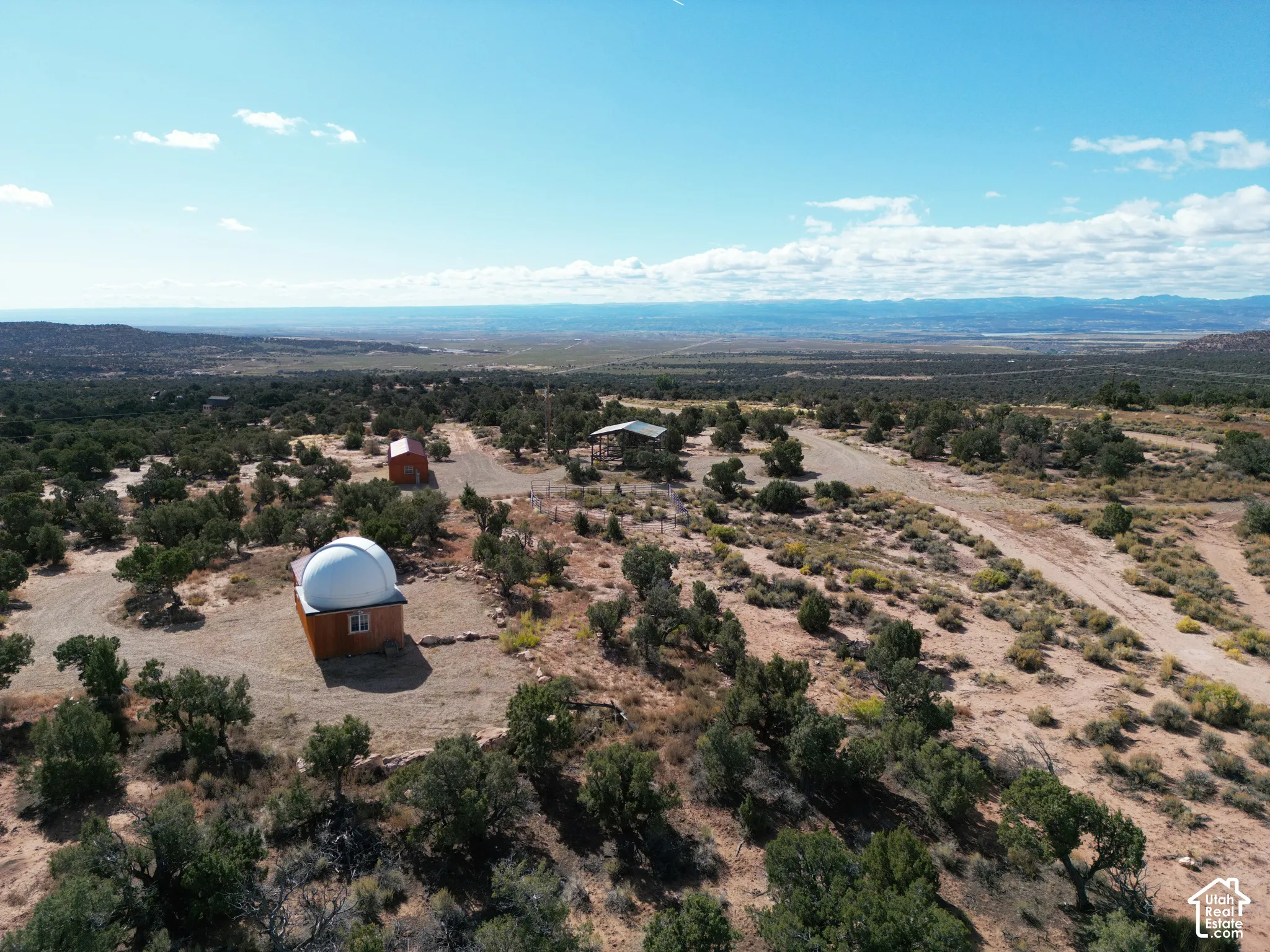 Expansive desert acreage featuring a structural observatory dome, secondary outbuilding, open-air metal-roofed shelter, and natural high-desert landscape