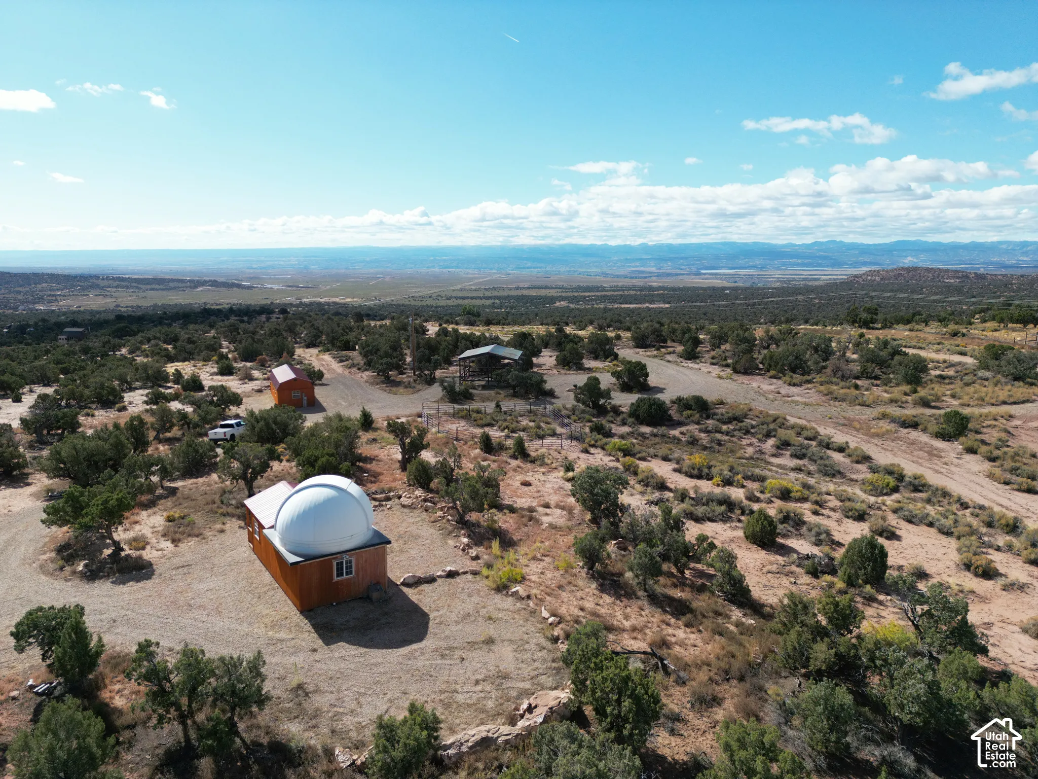 Expansive desert acreage featuring a custom observatory with a retractable dome, detached outbuildings, gravel access paths, and panoramic mountain backdrop