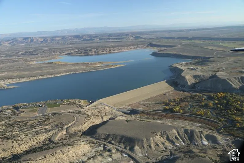 Aerial perspective featuring a large reservoir, earthen dam, desert terrain, and mountain backdrop