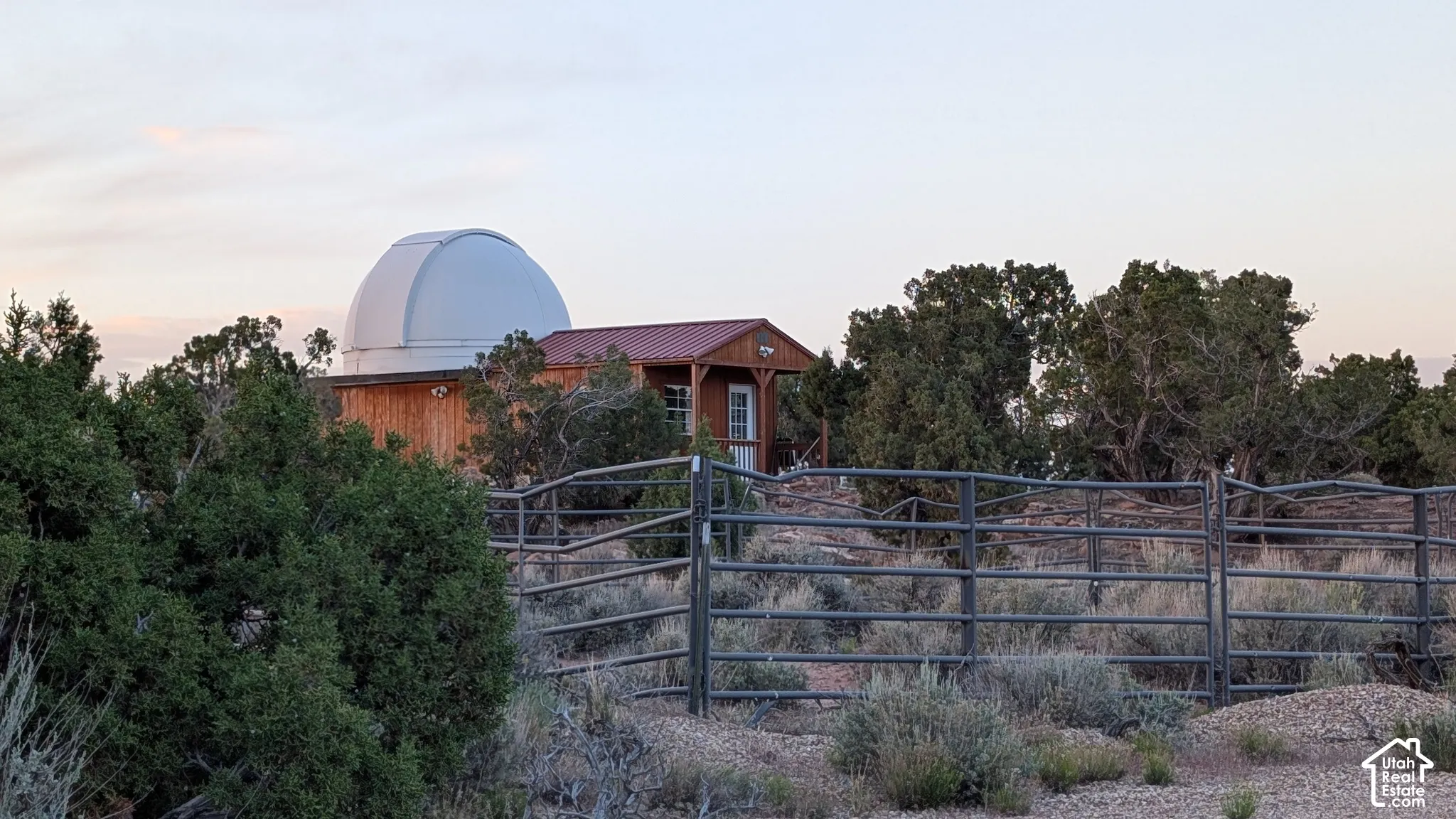 Observatory structure with a rotating dome, metal roof, wood-paneled exterior, and perimeter pipe fencing