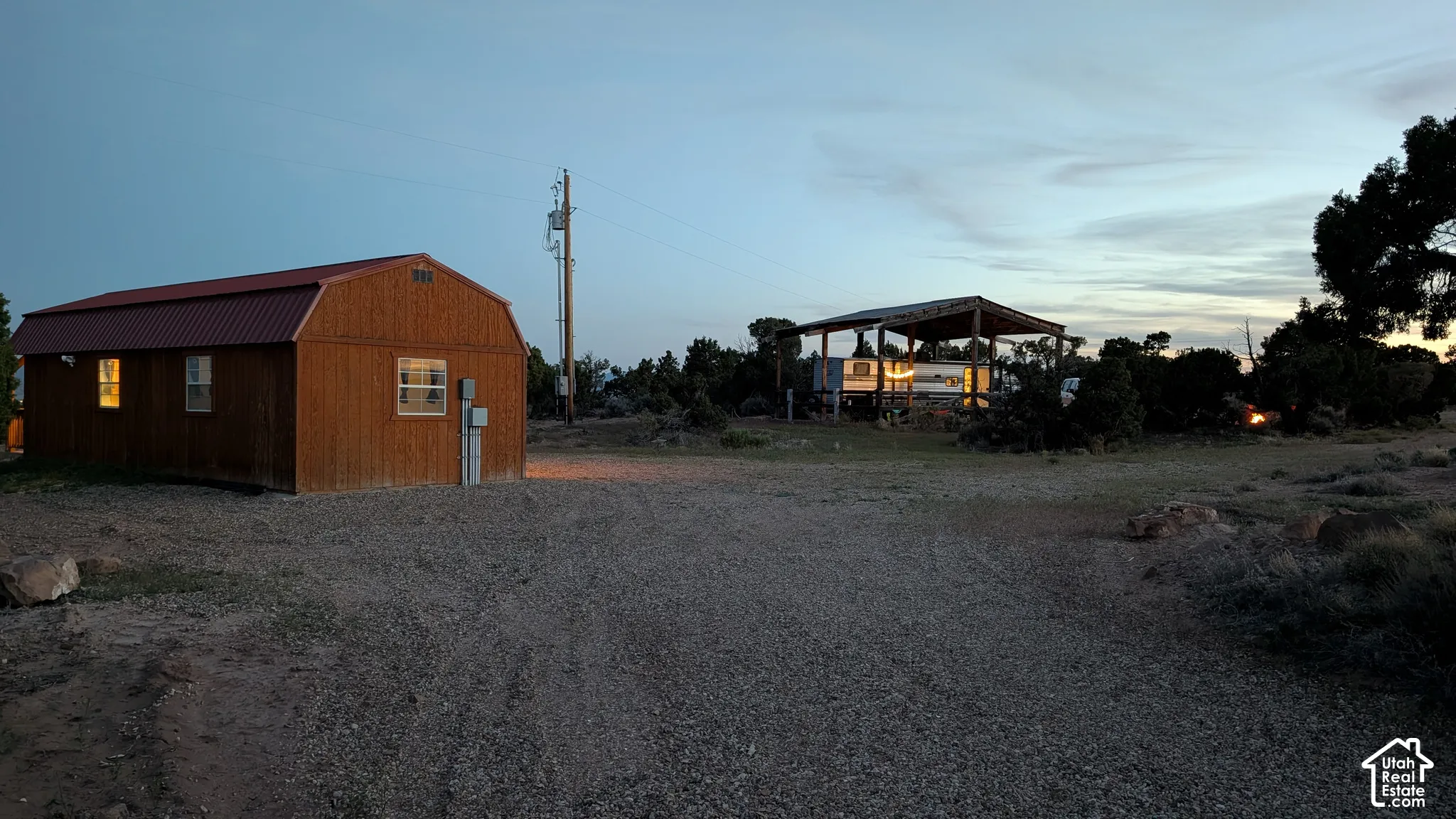 Barn-style structure with wood siding and a metal roof, accompanied by a detached metal-frame covered shelter situated on a gravel-surfaced lot