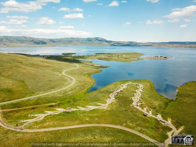 Aerial perspective of expansive waterfront acreage featuring paved roadways, designated parking areas, and mature landscape set against a mountain and lake backdrop