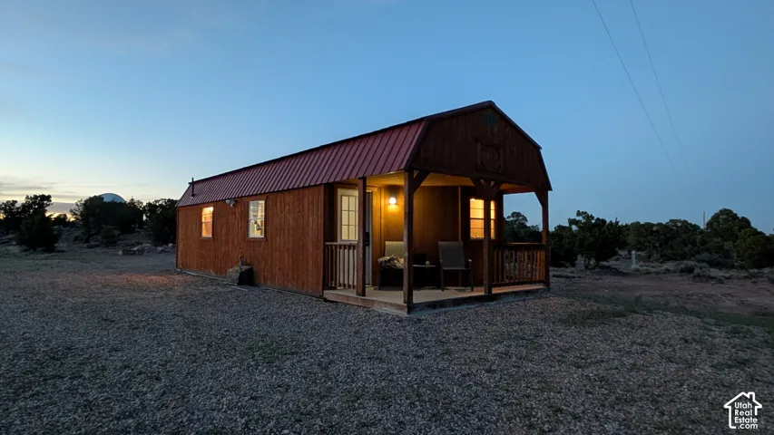 Wood-sided cabin featuring a gambrel roof with metal roofing, a covered porch with a wood railing, and multiple window placements