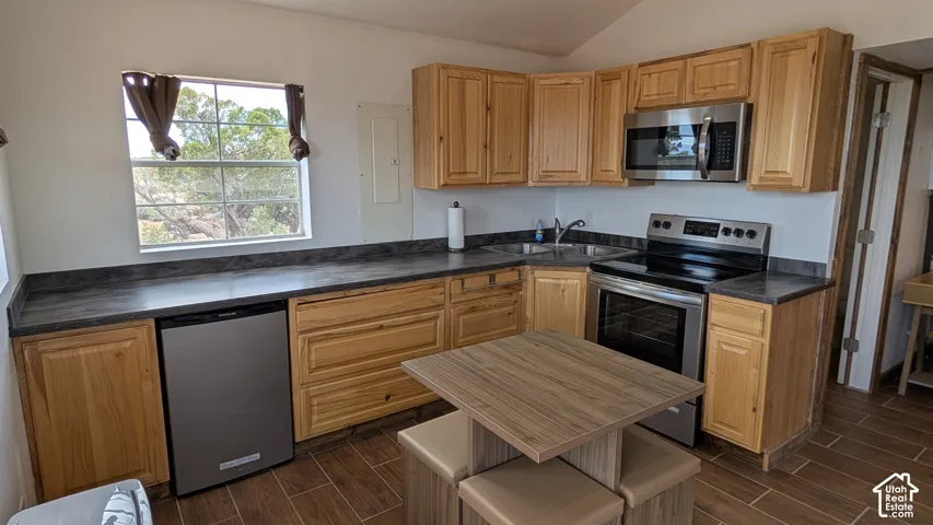 Kitchen featuring wood cabinetry, dark solid-surface countertops, stainless steel appliances, and wood-finish tile flooring