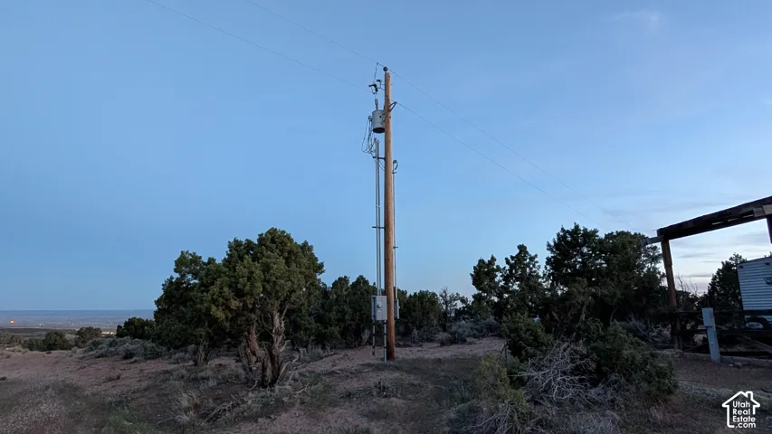 Utility pole with mounted electrical transformer, utility service box, and overhead power lines situated on a natural terrain lot with mature juniper trees