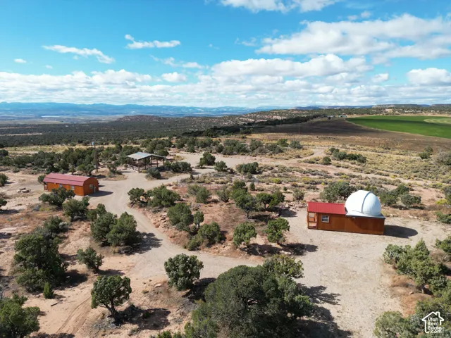 Aerial perspective of a sprawling property featuring multiple structures, including a wood-sided building with an integrated observatory dome, a detached rectangular outbuilding with a metal roof, an open-sided pavilion, and expansive native desert landsc