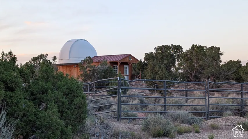 Observatory structure with a rotating dome, metal roof, wood-paneled exterior, and perimeter pipe fencing