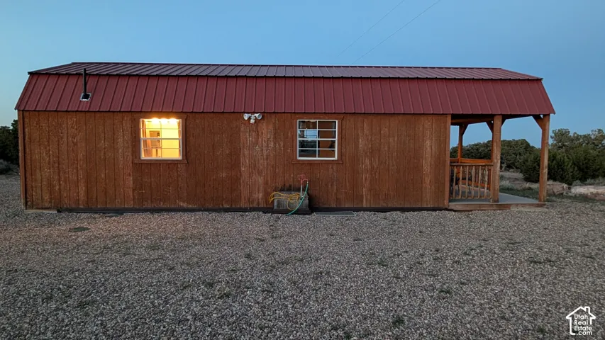 Single-story structure featuring wood-finish siding, a gambrel roofline with red metal roofing, a covered porch with wooden railings, and grid-pane windows
