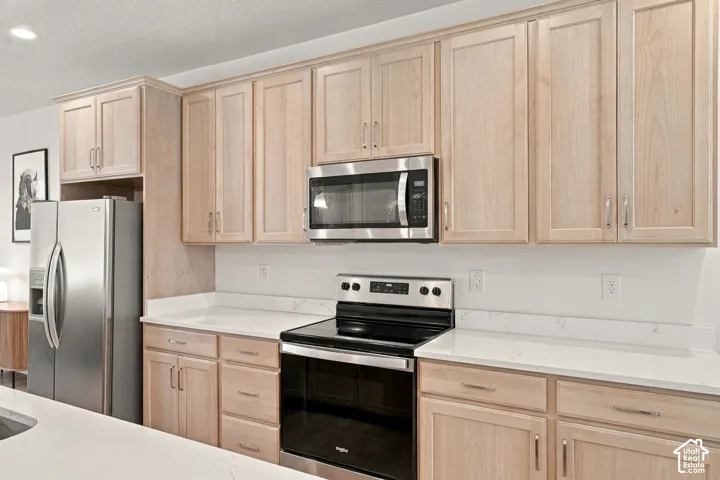 Natural-finish wood cabinetry featuring shaker-style doors, stone-surface countertops, and stainless steel appliances