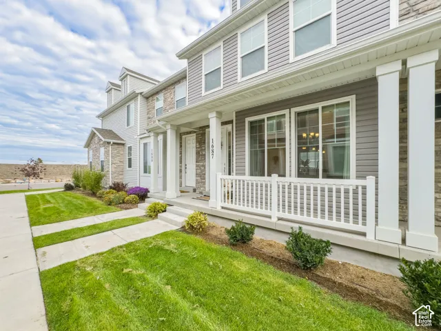 Multi-story exterior featuring gray horizontal siding, stone veneer accents, a covered front porch with white columns, and a white picket-style railing