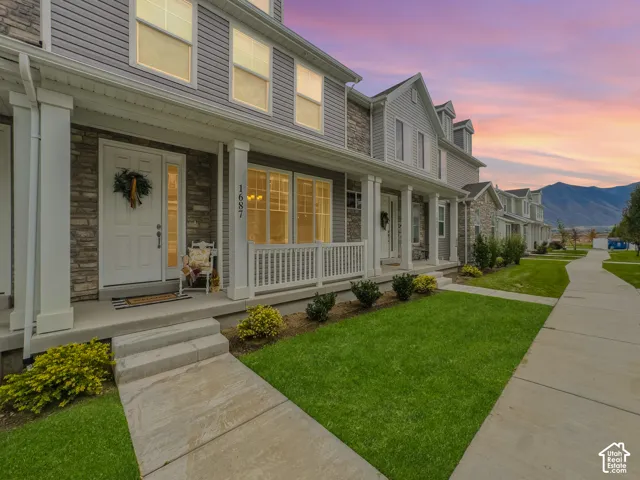 Multi-level exterior featuring light-gray horizontal siding, stone veneer accents, covered porches with square columns, and white railings