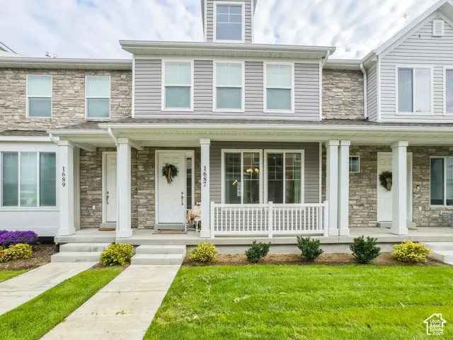 Multi-unit exterior featuring gray horizontal siding, stone veneer accents, a covered front porch with white columns, and a white balustrade railing
