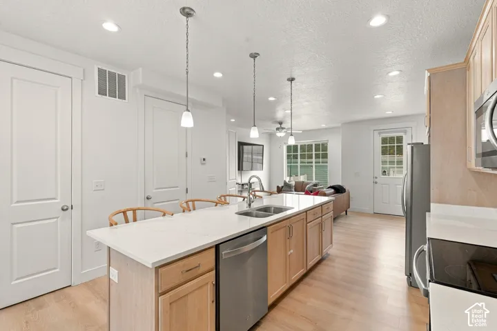 Kitchen featuring light-tone wood cabinetry, white stone-finish countertops, stainless steel appliances, recessed ceiling lighting, and three pendant lights