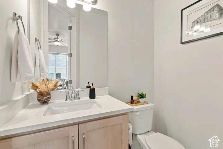 Vanity with light-toned cabinetry, white stone-composite countertop, integrated rectangular sink, chrome widespread faucet, and full-width mirror