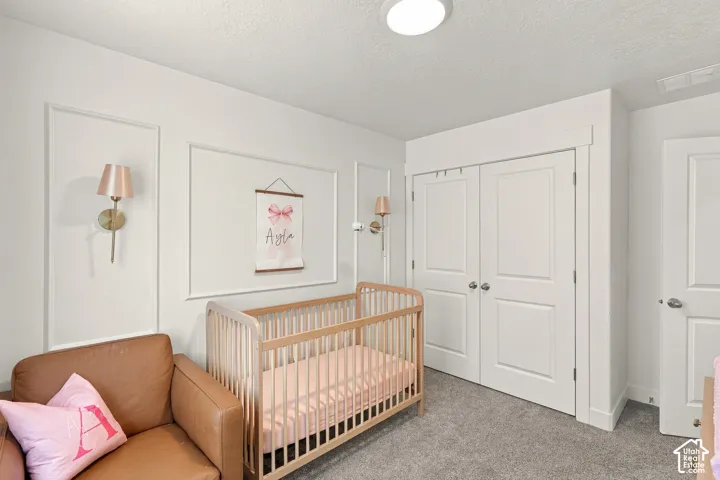 Interior room featuring walls with decorative trim molding, dual wall-mounted metallic light fixtures, double-door closet with shaker-style panels, and neutral carpeting