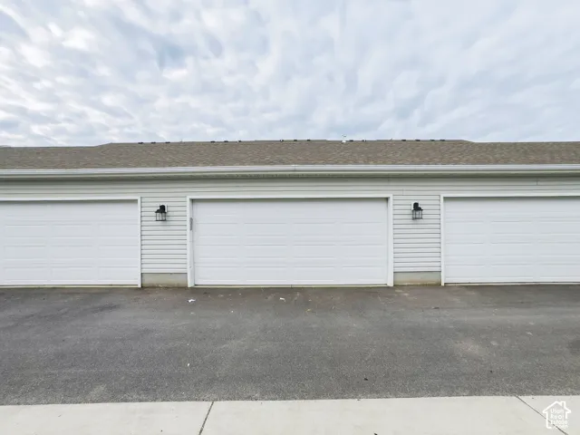 Triple-bay garage featuring horizontal siding, asphalt shingle roofing, and exterior wall-mounted lanterns