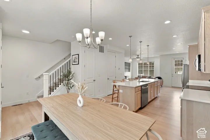 Kitchen featuring wood-finish cabinetry, central island with a stone-style countertop and integrated sink, recessed lighting, chandelier fixture, and wood-finish flooring