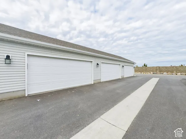 Three-car garage featuring white horizontal siding, asphalt shingles, and exterior wall-mounted lanterns