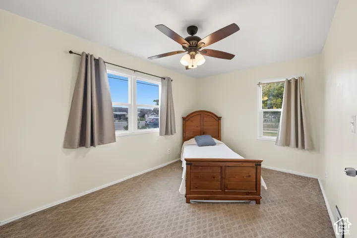 Bedroom featuring textured carpeting, dual-aspect vinyl windows, and a central ceiling fan with integrated light fixture