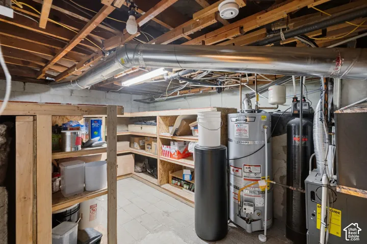 Utility area featuring built-in wooden shelving, a water heater, a water softener system, and an exposed beam ceiling