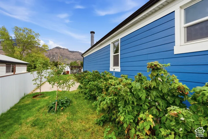 Exterior featuring horizontal blue siding, mountain backdrop, and metal perimeter fencing