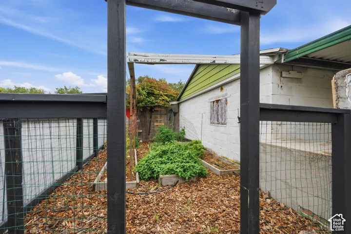 Exterior garden area featuring raised timber planting beds, a wire-mesh perimeter fence, and a black-painted wood frame entrance