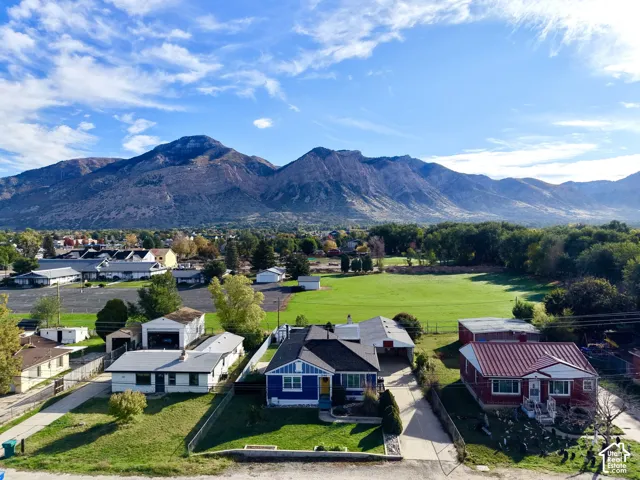 Aerial perspective featuring a single-story residence with a blue exterior, prominent mountain range backdrop, and expansive open green space