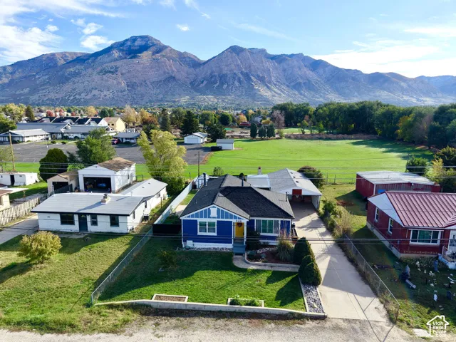 Single-story residence featuring a dark shingle roof, blue exterior siding with white decorative trim, a concrete driveway, an attached carport, and a prominent mountain backdrop