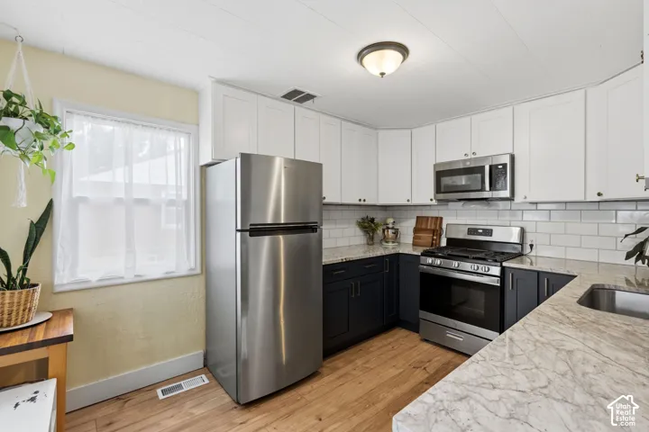 Kitchen featuring two-tone cabinetry, stone-patterned countertops, subway tile backsplash, stainless steel appliances, and wood-finish flooring