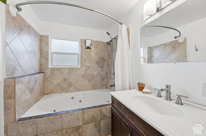Jetted soaking tub with diagonal tile surround, vanity with integrated basin, widespread metallic faucet, and wall-mounted vanity mirror