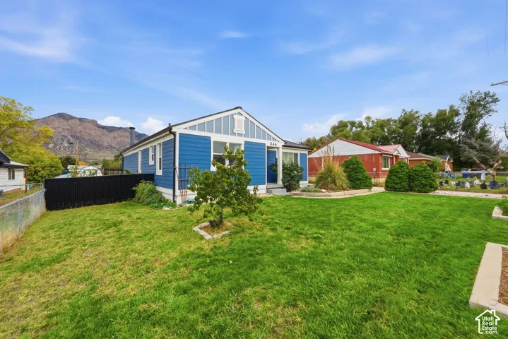 Blue-sided exterior featuring gable roofline, vertical board-and-batten siding accents, manicured front lawn, and prominent mountain backdrop