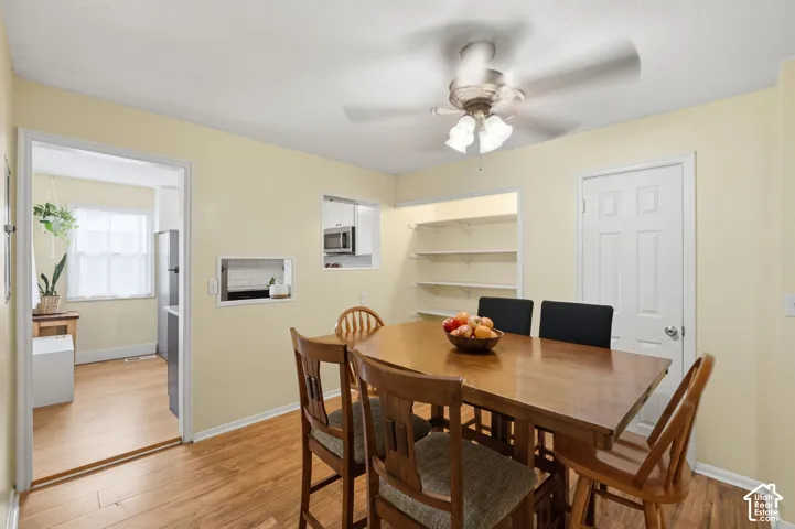 Dining area featuring wood-finish flooring, a ceiling fan with integrated lighting, built-in wall shelving, and two pass-through openings