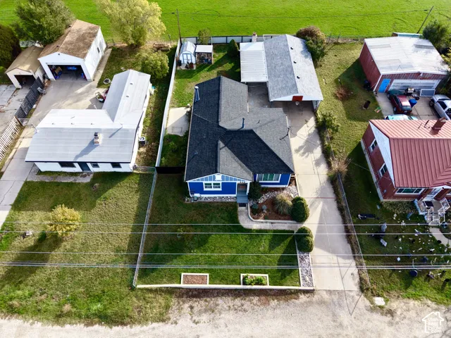 Aerial view of residential property featuring a detached garage, expansive concrete driveway, fenced yard, and a shingle roof