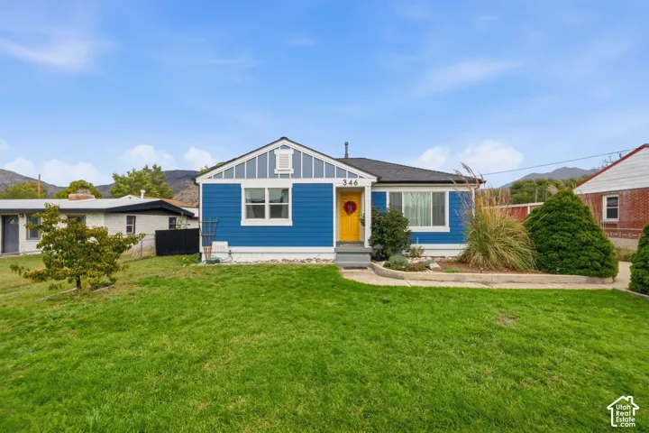 Blue siding exterior featuring a gable roof, decorative board-and-batten siding in the gable, contrasting yellow entry door, and a curved stone-bordered garden bed