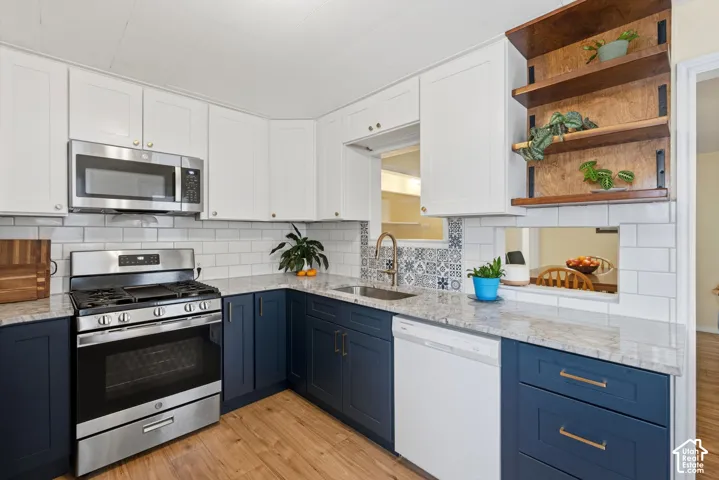 Kitchen featuring two-tone cabinetry, stone-finish countertops, stainless steel appliances, subway tile backsplash with decorative accents, and open wood shelving