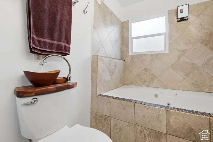 Jetted soaking tub with natural stone tile surround, vessel sink with curved chrome faucet, and live-edge wood vanity topper