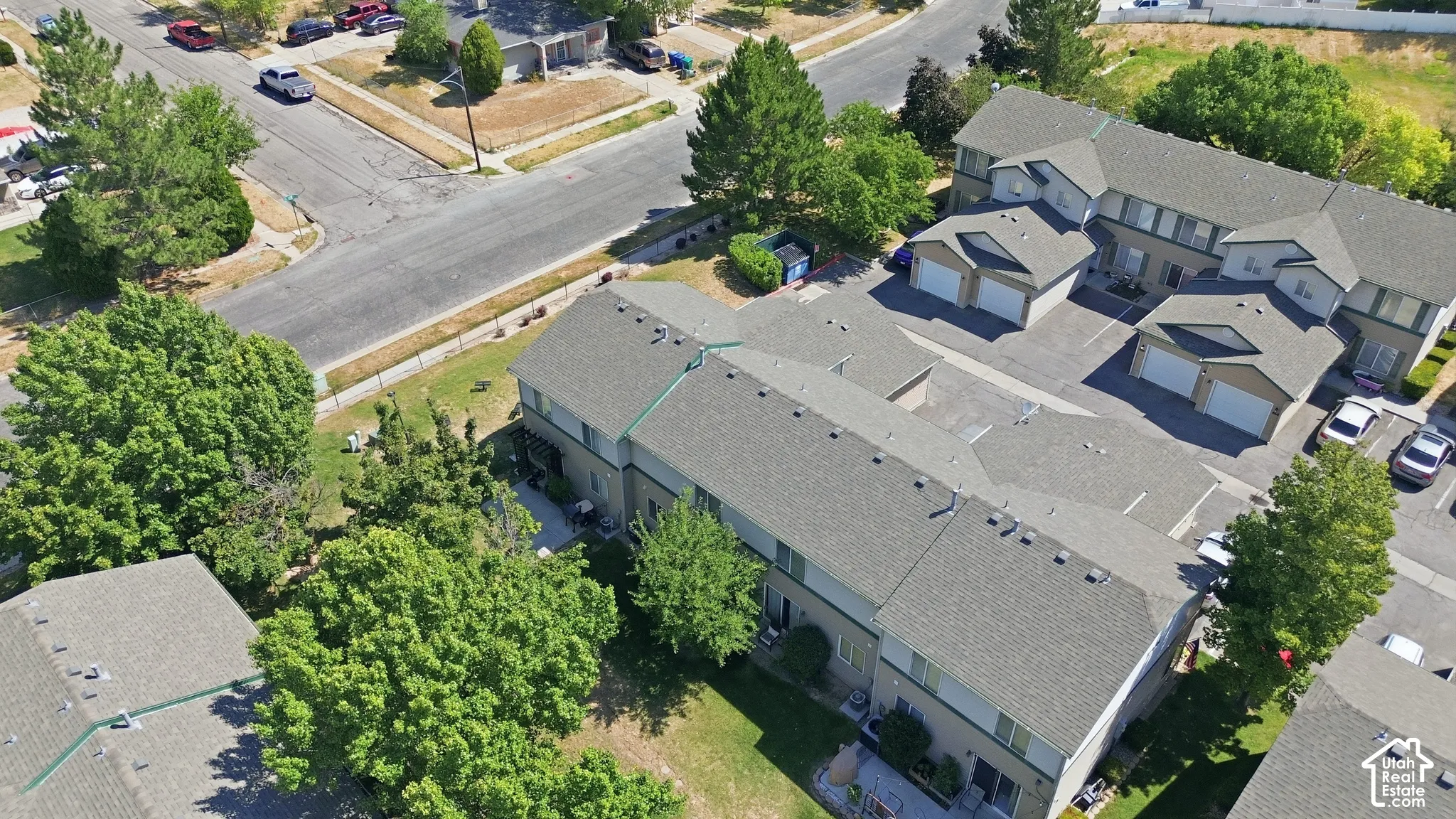 Aerial perspective of a multi-unit residential complex featuring asphalt shingle roofing, attached garage structures, paved driveways, and mature landscaping