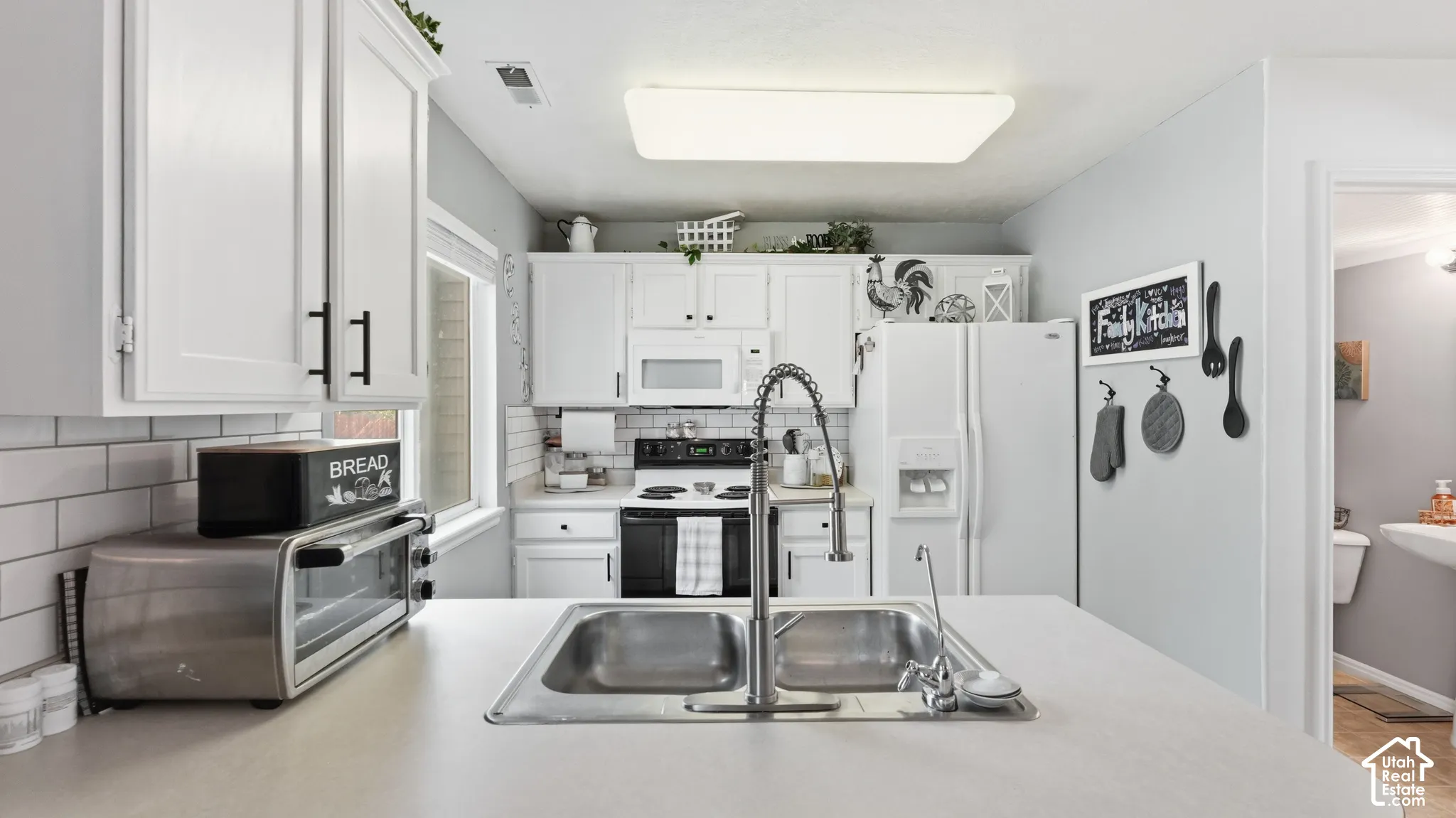 Kitchen featuring white cabinetry, a subway tile backsplash, solid-surface countertops, a stainless steel double-basin sink with a pull-down faucet, and a flat-panel flush-mount ceiling light