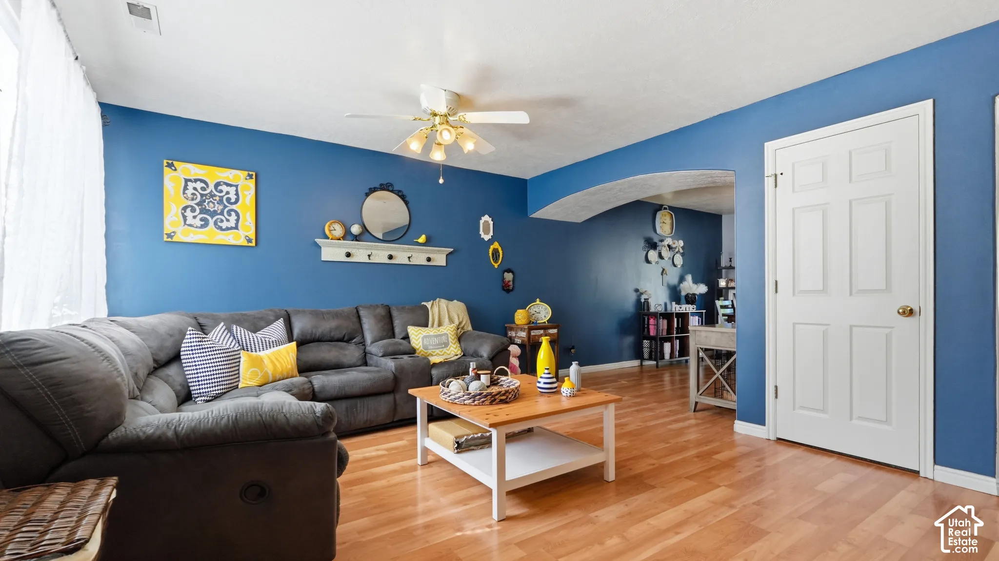 Living area featuring wood-finish flooring, a decorative arched entryway, and a multi-light ceiling fan
