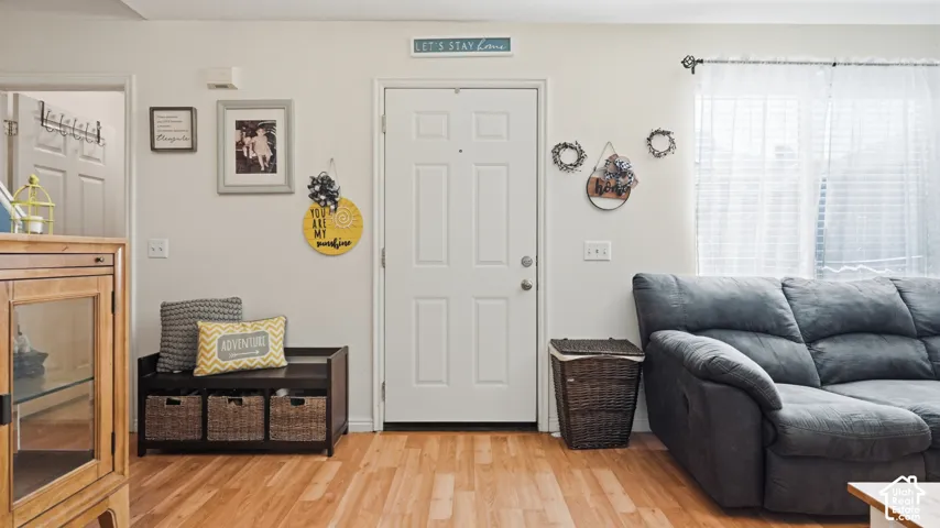 Six-panel exterior door with a peephole, neutral wall finishes, and wood-finish flooring