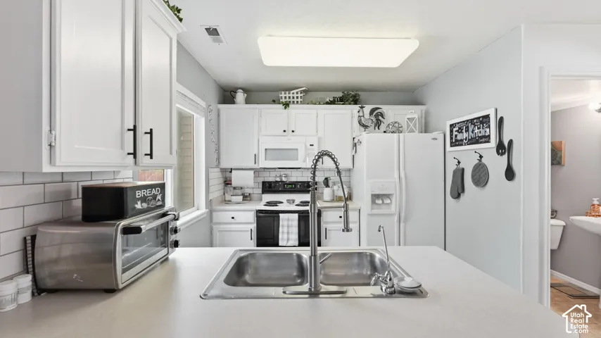 Kitchen featuring white cabinetry, a subway tile backsplash, solid-surface countertops, a stainless steel double-basin sink with a pull-down faucet, and a flat-panel flush-mount ceiling light