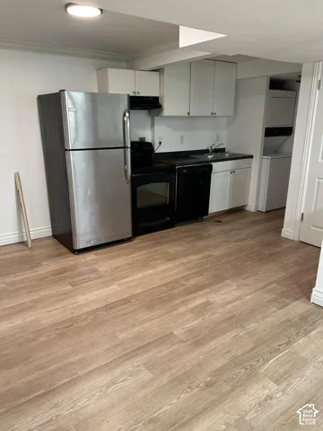 Kitchen area featuring wood-finish flooring, white cabinetry, a stainless steel refrigerator, black range, and an integrated laundry closet