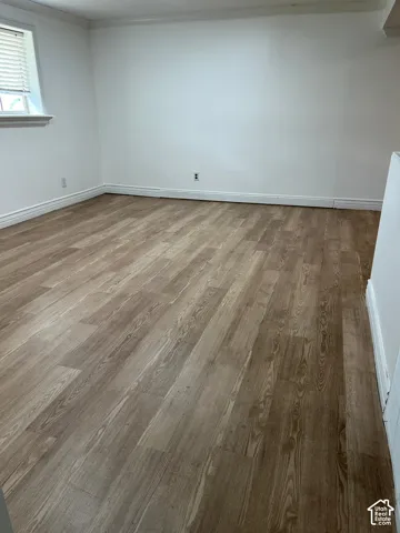 Neutral-toned interior space featuring wood-finish flooring, white walls, and a single window with blinds