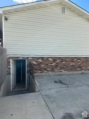 Exterior featuring horizontal siding, multi-tonal brick foundation, concrete paved area, and metal handrail