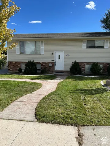 Split-level exterior featuring light horizontal siding, red brick masonry accents, a paved stone pathway, and multiple windows with white shutters