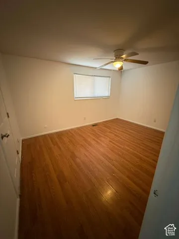 Room featuring wood-finish flooring, a ceiling fan with integrated lighting, and a window with horizontal blinds