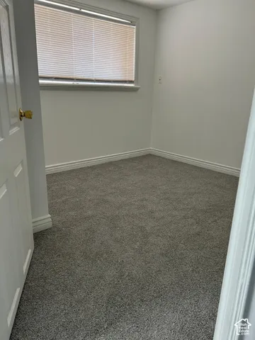 Room featuring neutral-toned carpeting, crisp white walls, and a window with horizontal blinds