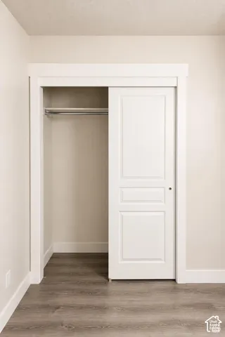 Reach-in closets in bedrooms, featuring a white paneled sliding door, wood-finish flooring, and a metal hanging rod with a shelf