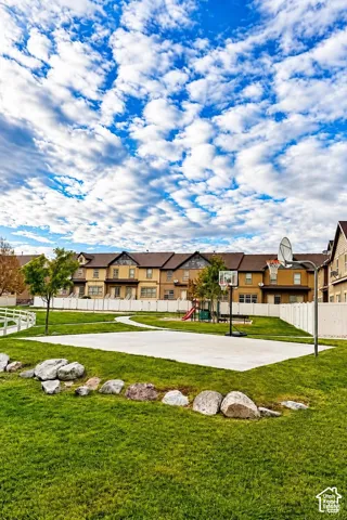 Common outdoor area featuring a paved basketball court, lawn, landscape boulders, and vinyl perimeter fencing