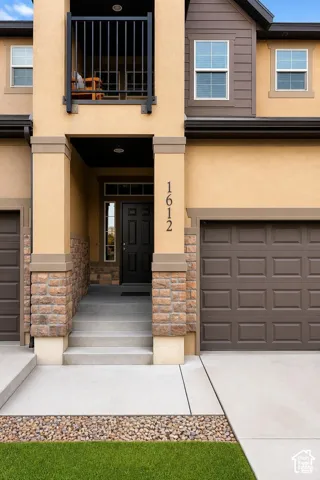Multi-story exterior featuring stucco, stone accents, recessed balcony with metal railing, and attached multi-car garage